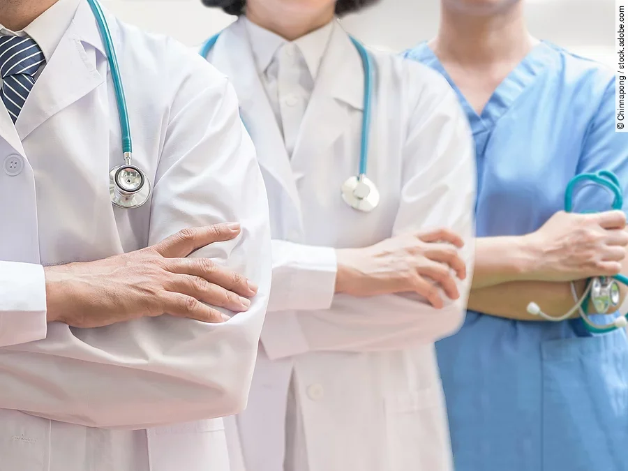 Klinikpersonal Drei Personen stehen nebeneinander. Links ein Arzt in weißem Kittel, in der Mitte eine Ärztin mit weißem Kittel, rechts eine Krankenschwester in blauem Kasack. Es sind jeweils nur die Torsi zu sehen. Alle drei haben ein Stethoskop.