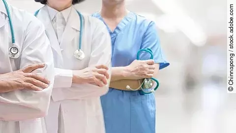 Drei Personen stehen nebeneinander. Links ein Arzt in weißem Kittel, in der Mitte eine Ärztin mit weißem Kittel, rechts eine Krankenschwester in blauem Kasack. Es sind jeweils nur die Torsi zu sehen. Alle drei haben ein Stethoskop.