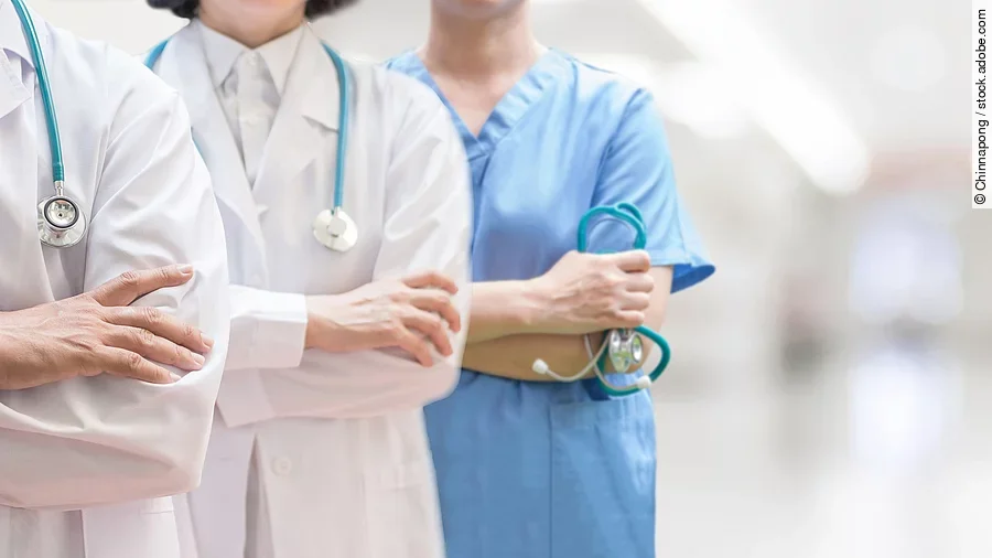 Klinikpersonal Drei Personen stehen nebeneinander. Links ein Arzt in weißem Kittel, in der Mitte eine Ärztin mit weißem Kittel, rechts eine Krankenschwester in blauem Kasack. Es sind jeweils nur die Torsi zu sehen. Alle drei haben ein Stethoskop.