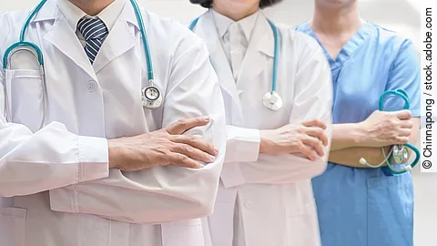 Drei Personen stehen nebeneinander. Links ein Arzt in weißem Kittel, in der Mitte eine Ärztin mit weißem Kittel, rechts eine Krankenschwester in blauem Kasack. Es sind jeweils nur die Torsi zu sehen. Alle drei haben ein Stethoskop.
