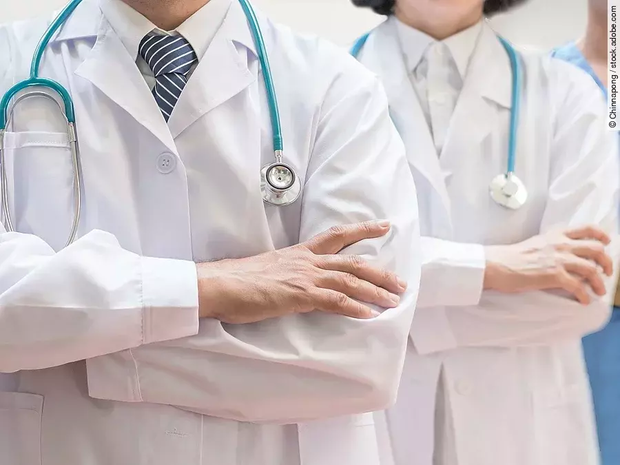 Drei Personen stehen nebeneinander. Links ein Arzt in weißem Kittel, in der Mitte eine Ärztin mit weißem Kittel, rechts eine Krankenschwester in blauem Kasack. Es sind jeweils nur die Torsi zu sehen. Alle drei haben ein Stethoskop.
