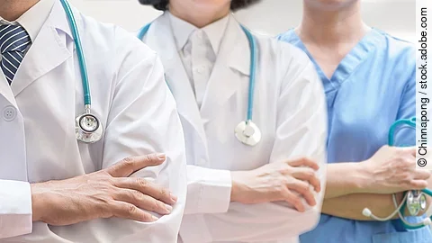 Klinikpersonal Drei Personen stehen nebeneinander. Links ein Arzt in weißem Kittel, in der Mitte eine Ärztin mit weißem Kittel, rechts eine Krankenschwester in blauem Kasack. Es sind jeweils nur die Torsi zu sehen. Alle drei haben ein Stethoskop.
