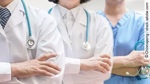 Drei Personen stehen nebeneinander. Links ein Arzt in weißem Kittel, in der Mitte eine Ärztin mit weißem Kittel, rechts eine Krankenschwester in blauem Kasack. Es sind jeweils nur die Torsi zu sehen. Alle drei haben ein Stethoskop.