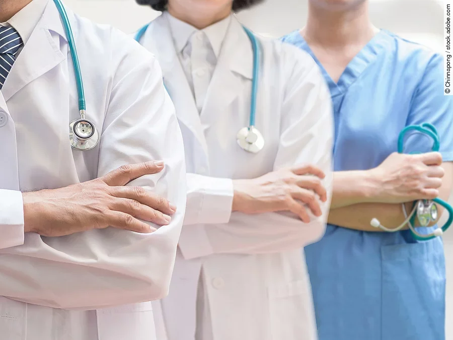 Klinikpersonal Drei Personen stehen nebeneinander. Links ein Arzt in weißem Kittel, in der Mitte eine Ärztin mit weißem Kittel, rechts eine Krankenschwester in blauem Kasack. Es sind jeweils nur die Torsi zu sehen. Alle drei haben ein Stethoskop.
