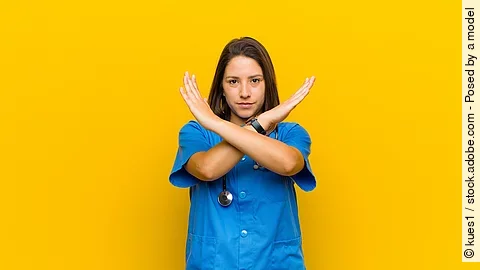 Stop Krankenpflegerin vor gelbem Hintergrund die die Arme verkreuzt um Stop zu zeigen