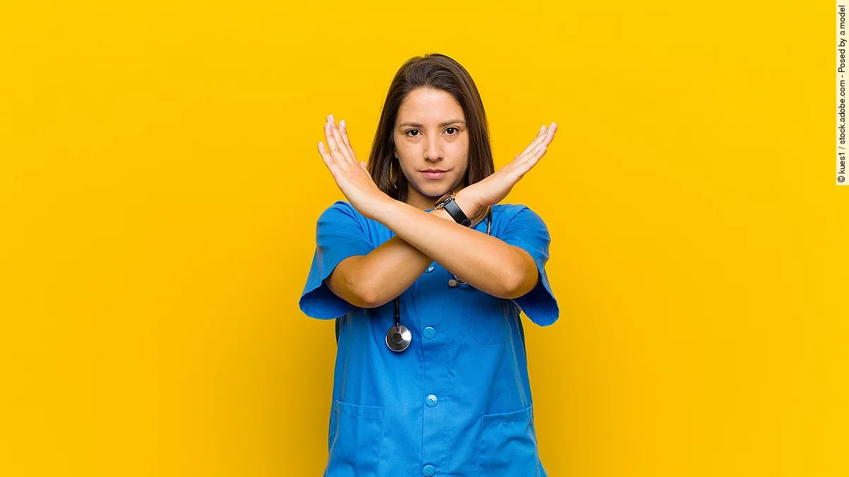 Krankenpflegerin vor gelbem Hintergrund die die Arme verkreuzt um Stop zu zeigen
