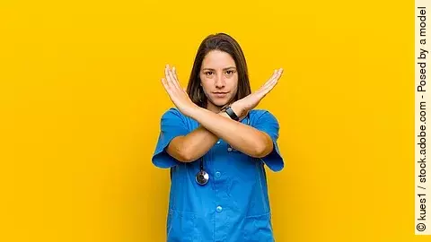 Krankenpflegerin vor gelbem Hintergrund die die Arme verkreuzt um Stop zu zeigen