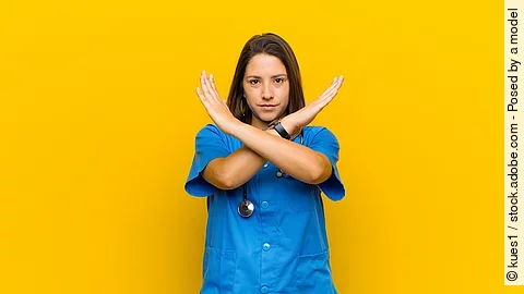 Stop Krankenpflegerin vor gelbem Hintergrund die die Arme verkreuzt um Stop zu zeigen