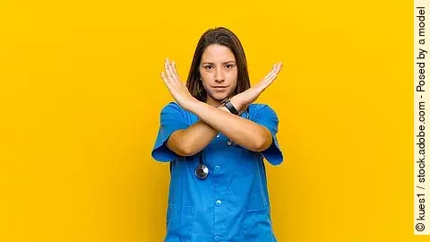 Krankenpflegerin vor gelbem Hintergrund die die Arme verkreuzt um Stop zu zeigen