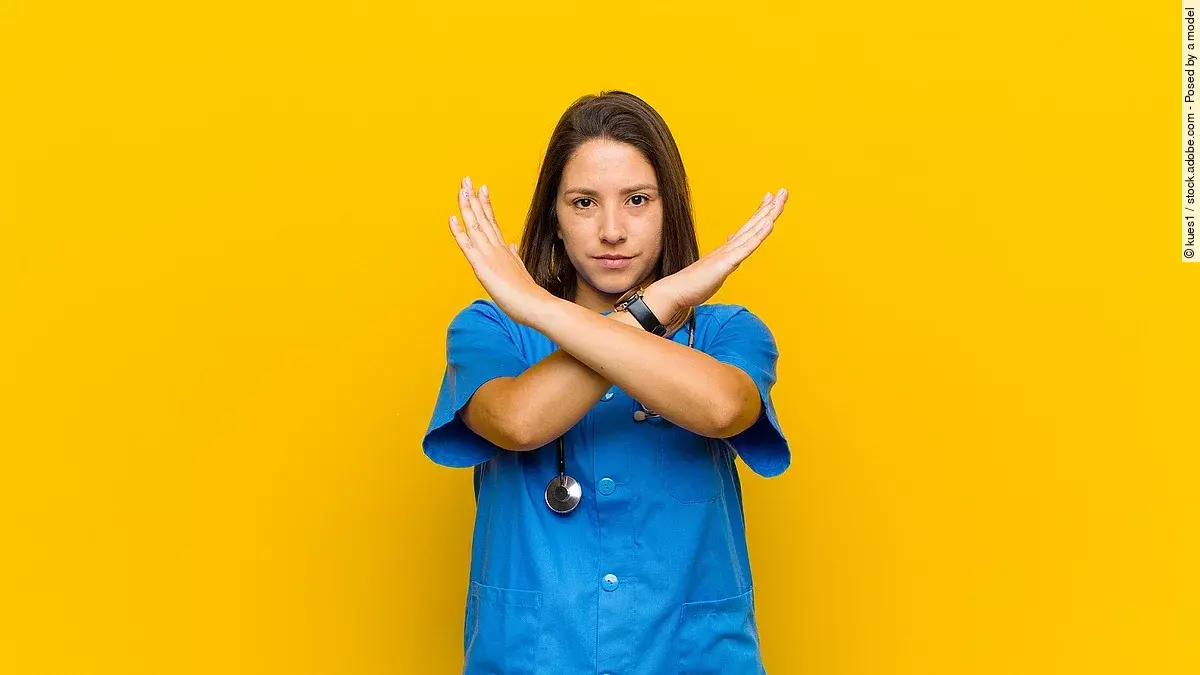 Stop Krankenpflegerin vor gelbem Hintergrund die die Arme verkreuzt um Stop zu zeigen