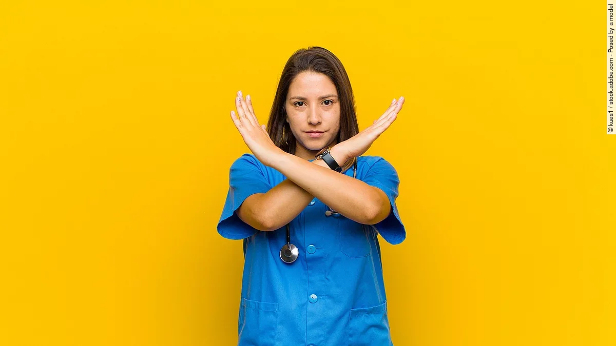 Krankenpflegerin vor gelbem Hintergrund die die Arme verkreuzt um Stop zu zeigen