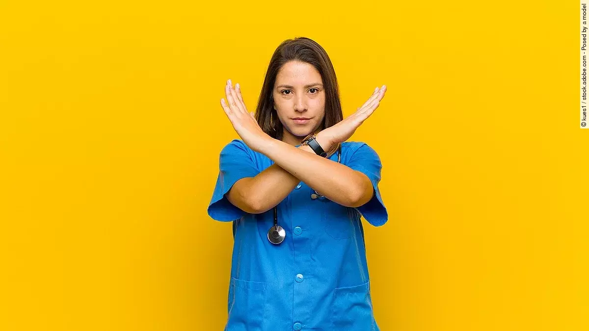 Krankenpflegerin vor gelbem Hintergrund die die Arme verkreuzt um Stop zu zeigen
