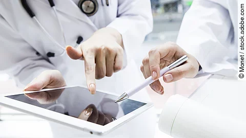 Zwei Ärzte in weißen Kitteln bearbeiten etwas auf einem Tablet.