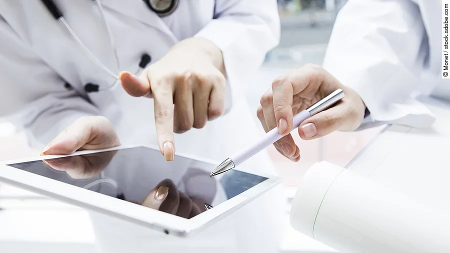 E-Health Zwei Ärzte in weißen Kitteln bearbeiten etwas auf einem Tablet.