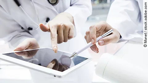 Zwei Ärzte in weißen Kitteln bearbeiten etwas auf einem Tablet.