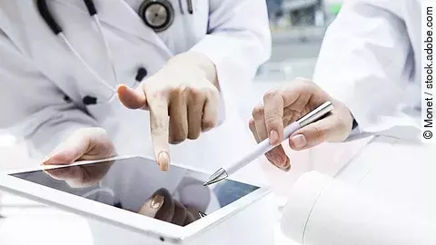 E-Health Zwei Ärzte in weißen Kitteln bearbeiten etwas auf einem Tablet.