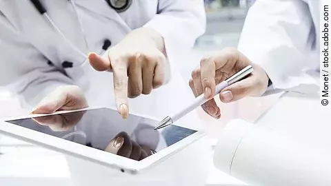 Zwei Ärzte in weißen Kitteln bearbeiten etwas auf einem Tablet.