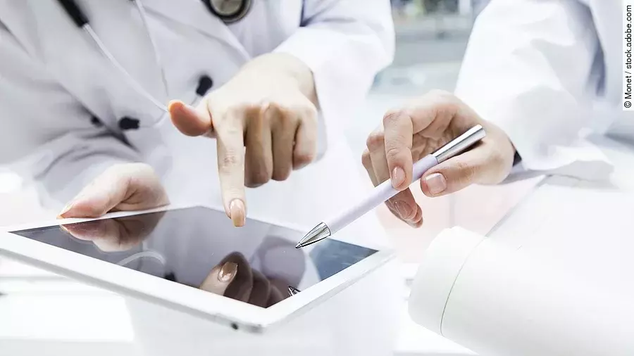 Zwei Ärzte in weißen Kitteln bearbeiten etwas auf einem Tablet.