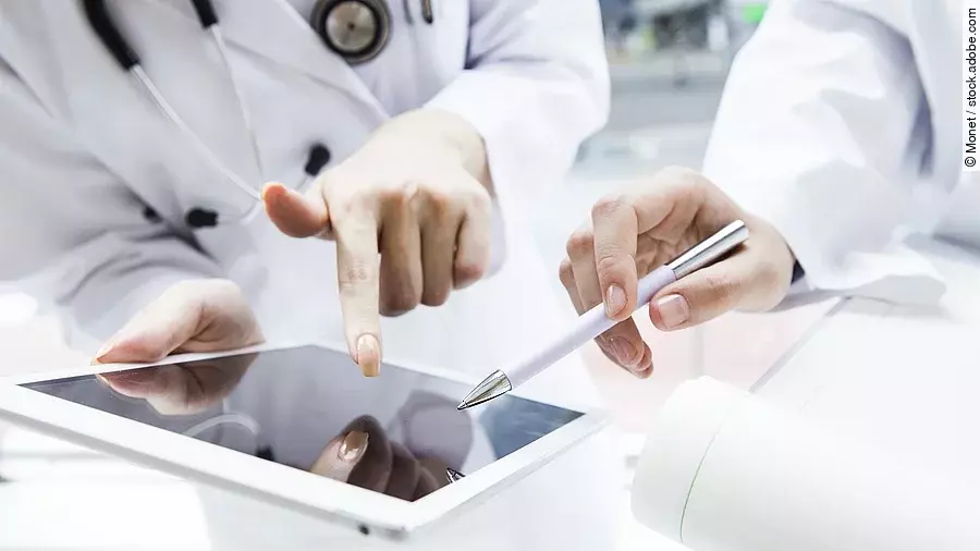 E-Health Zwei Ärzte in weißen Kitteln bearbeiten etwas auf einem Tablet.