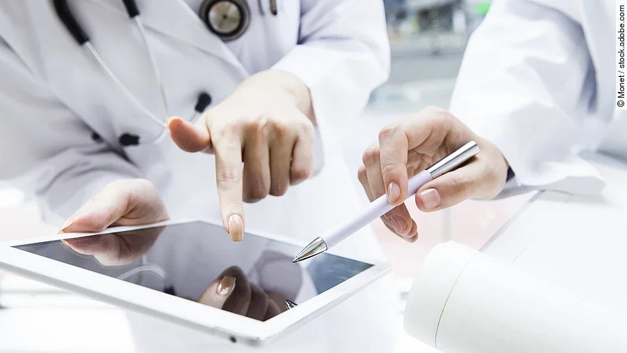 Zwei Ärzte in weißen Kitteln bearbeiten etwas auf einem Tablet.