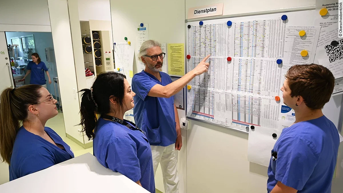 Vier Menschen stehen vor einem Dienstplan in einem Krankenhaus.