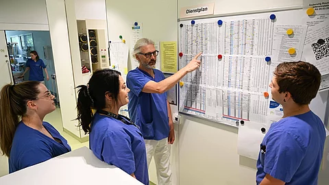 Vier Menschen stehen vor einem Dienstplan in einem Krankenhaus.