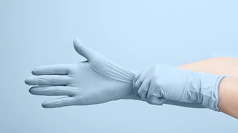 Eine Person zieht hellblaue Einweghandschuhe über.