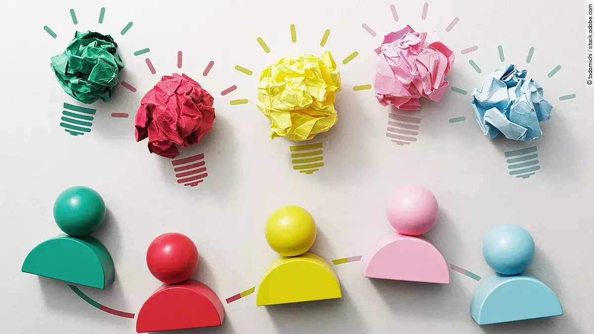 Fünf verschiedenfarbige Holzfiguren nebeneinender, darüber Glühbirnen aus Papier