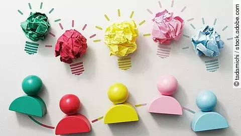 Fünf verschiedenfarbige Holzfiguren nebeneinender, darüber Glühbirnen aus Papier