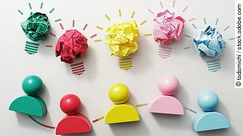 Fünf verschiedenfarbige Holzfiguren nebeneinender, darüber Glühbirnen aus Papier