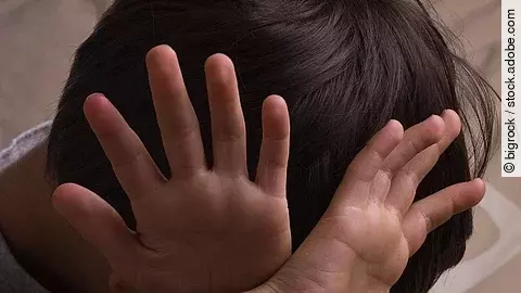 Ein Kind hält sich abwehrend die Hände vors Gesicht.