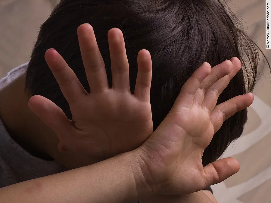 Ein Kind hält sich abwehrend die Hände vors Gesicht.