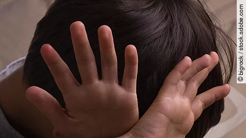 Kind Ein Kind hält sich abwehrend die Hände vors Gesicht.