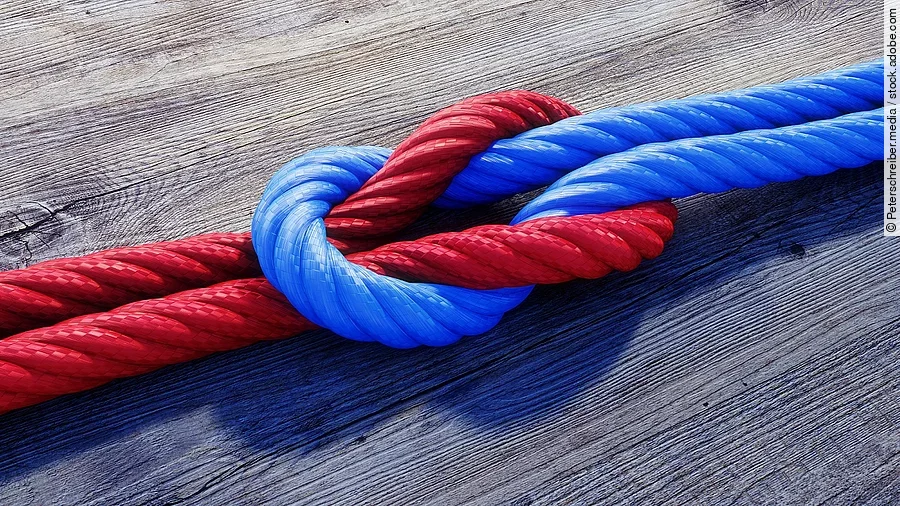 Ein rotes und ein blaues Seil bilden einen Kreuzknoten.