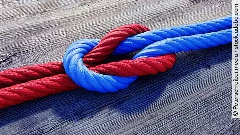 Ein rotes und ein blaues Seil bilden einen Kreuzknoten.