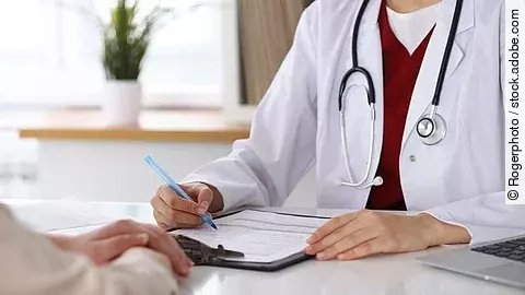 Ärztin füllt Formular aus und sitzt gegenüber eines Patienten.