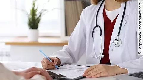 Ärztin füllt Formular aus und sitzt gegenüber eines Patienten.