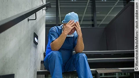 Ein Arzt sitzt nach einer OP verzweifelt auf einer Treppe.