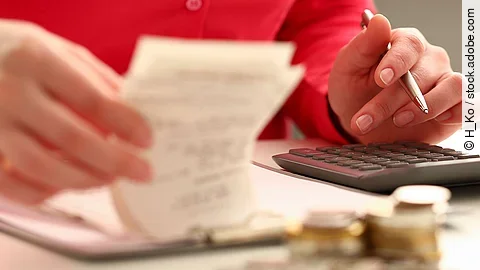 Rechnung Person sitzt an einem Tisch und bearbeitet Rechnungen. Auf dem Tisch steht ein Sparschwein und ein Stapel Münzen.