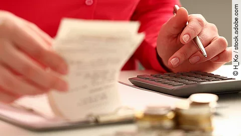 Rechnung Person sitzt an einem Tisch und bearbeitet Rechnungen. Auf dem Tisch steht ein Sparschwein und ein Stapel Münzen.