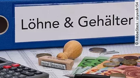 Ein dicker Ordner, auf dem "Löhne & Gehälter" steht. Davor liegen ein Taschenrechner, einige Geldscheine, ein Stempel und ein Kugelschreiber.