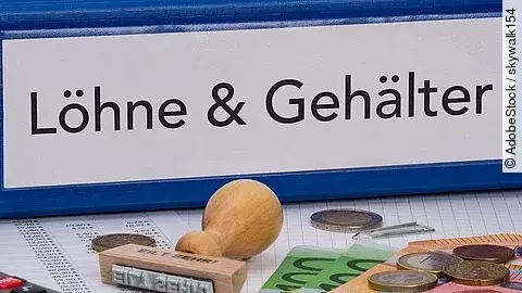 Ein dicker Ordner, auf dem "Löhne & Gehälter" steht. Davor liegen ein Taschenrechner, einige Geldscheine, ein Stempel und ein Kugelschreiber.