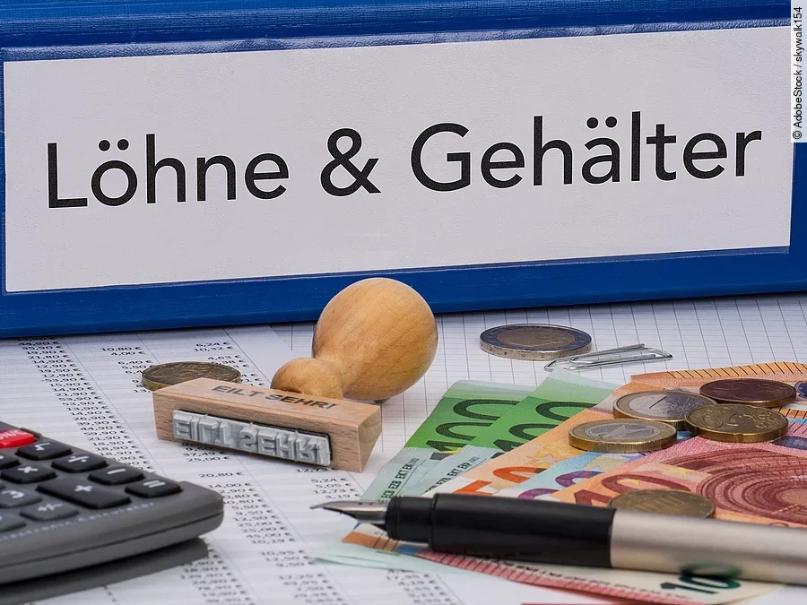 Gehalt Ein dicker Ordner, auf dem "Löhne & Gehälter" steht. Davor liegen ein Taschenrechner, einige Geldscheine, ein Stempel und ein Kugelschreiber.