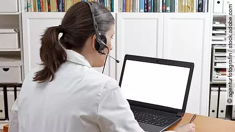 Videosprechstunde Eine Ärztin sitzt mit Headset vor einem Laptop und führt eine Tele-Sprechstunde durch.