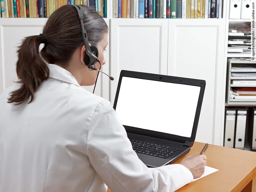 Videosprechstunde Eine Ärztin sitzt mit Headset vor einem Laptop und führt eine Tele-Sprechstunde durch.