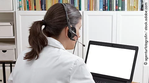 Eine Ärztin sitzt mit Headset vor einem Laptop und führt eine Tele-Sprechstunde durch. 