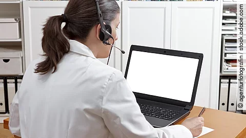 Eine Ärztin sitzt mit Headset vor einem Laptop und führt eine Tele-Sprechstunde durch. 