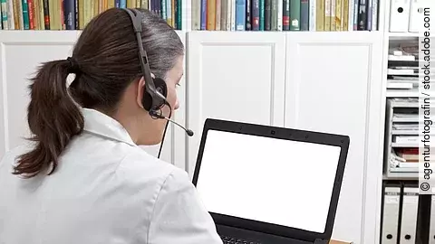 Eine Ärztin sitzt mit Headset vor einem Laptop und führt eine Tele-Sprechstunde durch. 