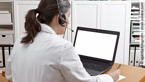 Eine Ärztin sitzt mit Headset vor einem Laptop und führt eine Tele-Sprechstunde durch. 