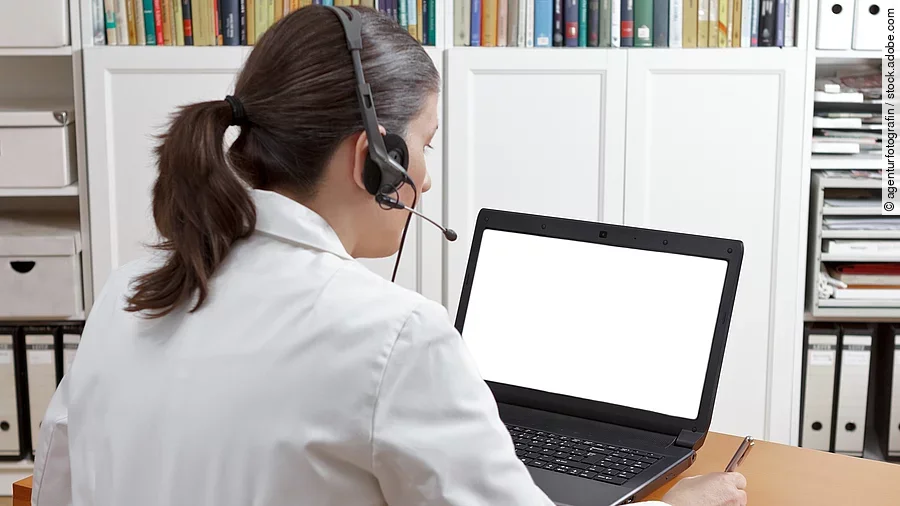 Eine Ärztin sitzt mit Headset vor einem Laptop und führt eine Tele-Sprechstunde durch. 
